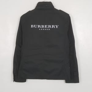 以下が含まれることがあります： 背中に白で「BURBERRY LONDON」とプリントされた黒いジャケット。 ジャケットは襟付き、長袖、ボタンダウンフロントです。 ジャケットは無地の黒色です。