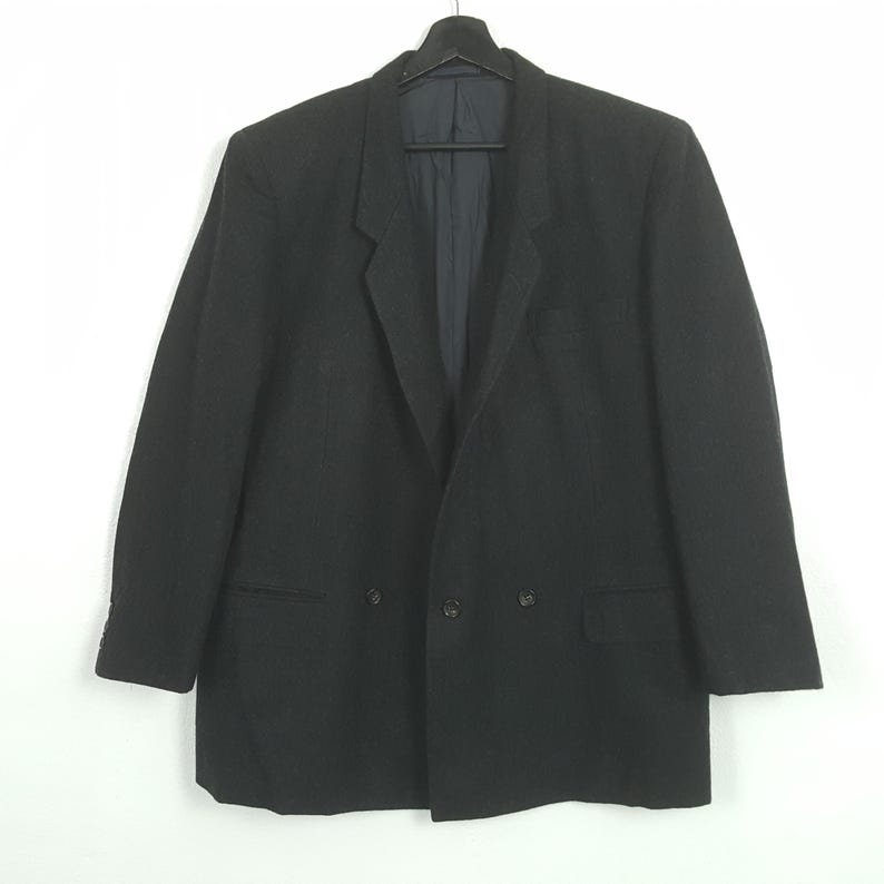 May include: A black double-breasted blazer with a notched lapel, two rows of buttons, and two front pockets. The blazer is hanging on a black hanger against a white background. The jacket has a classic, tailored design.