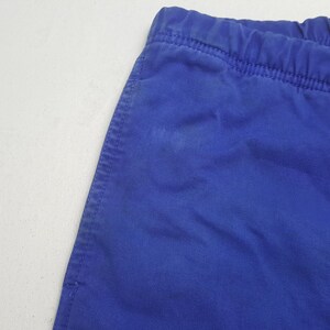 Puede incluir: Primer plano de una secci&oacute;n de tela azul, posiblemente pantalones cortos o pantalones. La tela tiene una textura visible y una costura cosida a lo largo del borde. La cintura es el&aacute;stica. El fondo es una superficie blanca lisa.