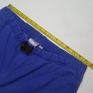 Puede incluir: Primer plano de pantalones azules con cintura el&aacute;stica y hebilla negra. Una cinta m&eacute;trica amarilla muestra la longitud en cent&iacute;metros. Los pantalones tienen una peque&ntilde;a etiqueta que dice "USA".