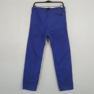 Puede incluir: Un pantal&oacute;n azul colgado de una percha negra. El pantal&oacute;n es de color azul liso y parece estar hecho de una tela duradera. La parte trasera del pantal&oacute;n es visible, mostrando la cintura y un peque&ntilde;o logotipo.