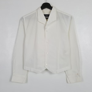 May include: A white, long-sleeved shirt with a unique collar and button-down front. The shirt has a tailored fit and is made of a lightweight fabric. The cuffs are buttoned. The shirt is hanging on a black hanger.