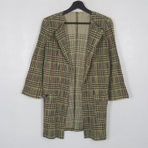 Puede incluir: Una chaqueta de manga larga abierta por delante con un patrón de cuadros en marrón, beige y verde. La prenda tiene un dobladillo recto, un escote sin cuello y un forro interior visible que muestra una versión más clara y tenue del diseño exterior.