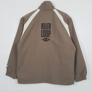 Op de afbeelding: Bruine jas met witte schouderstrepen en de zwarte tekst "KILLER LOOP" op de rug. Het heeft een hoge kraag en een ritssluiting. Een klein logo is zichtbaar op de linkermouw. Een casual bovenkledingstuk.