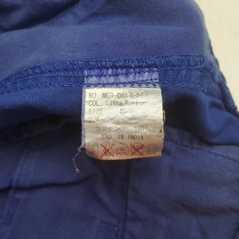 Puede incluir: Primer plano de una prenda azul con una etiqueta. La etiqueta muestra texto que incluye "Ultra Marine" y "100% algod&oacute;n". La prenda es de color azul liso. La etiqueta tambi&eacute;n indica que el art&iacute;culo fue fabricado en India.
