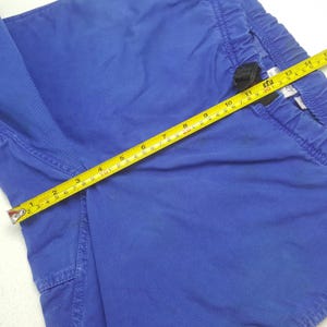 Puede incluir: Primer plano de unos pantalones cortos azules con cintura con cord&oacute;n. Una cinta m&eacute;trica amarilla se coloca sobre los pantalones cortos, mostrando medidas en cent&iacute;metros. Los pantalones cortos tienen un peque&ntilde;o bolsillo lateral.