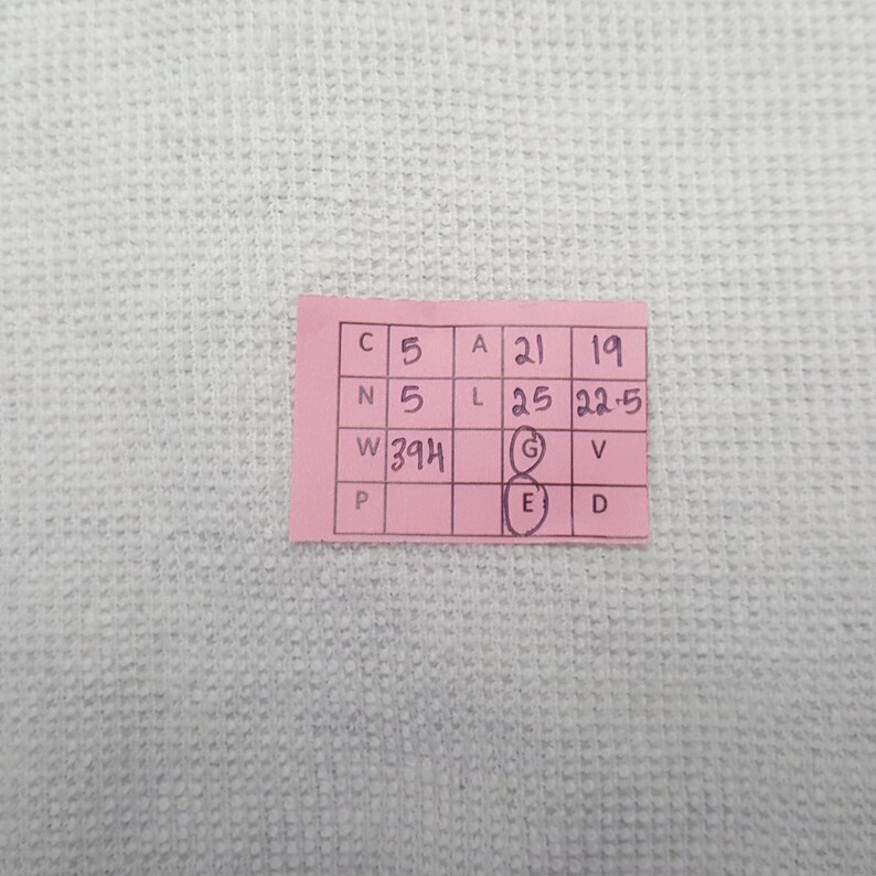 May include: A small pink tag with black text and numbers, including "W394". The tag is on a white, textured surface. The text is arranged in a grid format, with letters and numbers in each cell.