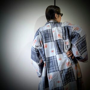 Peut inclure: Une chemise à manches longues boutonnée présentant un motif de style patchwork avec des carrés alternés de tartan gris foncé et de tissu gris clair. Les sections gris clair sont ornées de petits motifs floraux orange et de points blancs.