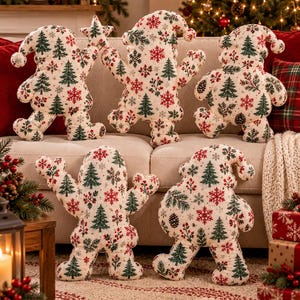 Peut inclure: Cinq coussins décoratifs en peluche en forme de gnomes, chacun doté d'un tissu crème avec un motif répétitif de sapins verts, de flocons de neige rouges et de baies. Les gnomes ont des corps arrondis, des bras et des chapeaux pointus.