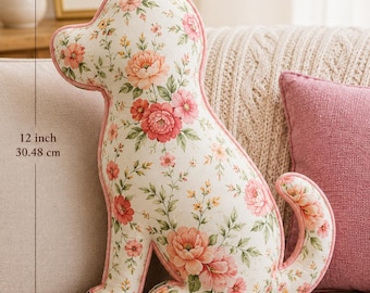 May include: A dog-shaped decorative pillow featuring a cream fabric with a pink and orange floral pattern and green leaves. The pillow has pink piping along the edges and measures 12 inches in height and 8 inches in width as indicated by arrows.