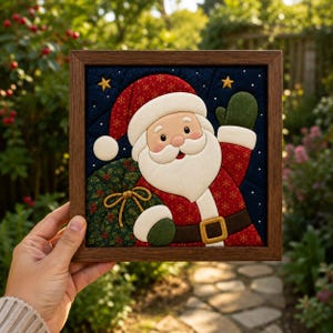 May include: A square framed fabric wall art piece featuring a quilted Santa Claus with a red hat, white beard, and green mittens. Santa holds a green sack with a gold ribbon against a dark blue background with gold stars and white dots.