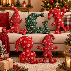 May include: Five plush elf-shaped pillows featuring festive holiday patterns. Three are red with white snowflakes and holly, one is green with white snowflakes and holly, and one is red with white snowflakes and small green Christmas trees.