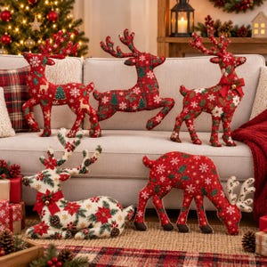 Pode incluir: Cinco decorações de rena de pelúcia com padrões festivos. Três renas em pé exibem tecido vermelho com flocos de neve brancos, azevinho verde e detalhes dourados. Uma rena creme está deitada com poinsétias, enquanto outra vermelha pasta.