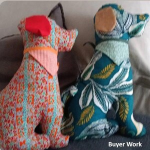 以下が含まれることがあります： 布製の犬のぬいぐるみ2体。左側の犬は鮮やかなオレンジと青の柄生地で、赤い耳とピーチ色のバンダナを巻いています。右側の犬は白の葉柄が入ったティール色の生地で、タン色の耳とライトグリーンのバンダナを巻いています。