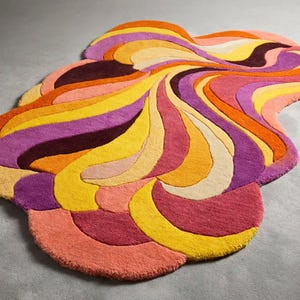 May include: An irregularly shaped area rug featuring a vibrant, multi-colored pattern of swirling, organic waves. The design incorporates shades of bright orange, deep purple, sunny yellow, soft pink, and cream in a flowing, layered composition.