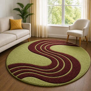 May include: A round area rug with a green background and a wavy, burgundy pattern. The rug is placed on a hardwood floor in a living room setting, with a sofa, chair, and window visible in the background.