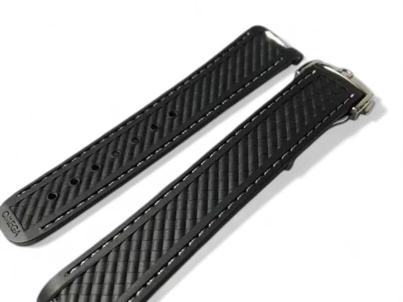 K&ouml;nnte beinhalten: Zwei schwarze Uhrenarmb&auml;nder mit strukturiertem Muster und wei&szlig;en N&auml;hten. Eines der Armb&auml;nder hat eine Schnalle, das andere hat Einstelll&ouml;cher. Das Wort "OMEGA" ist auf einem Armband sichtbar.