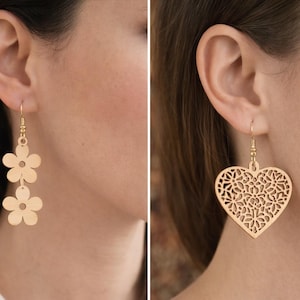 May include: Gold-colored earrings in two styles: one with two flower shapes, the other with a heart-shaped filigree design. The earrings are hanging from the ear of a person.