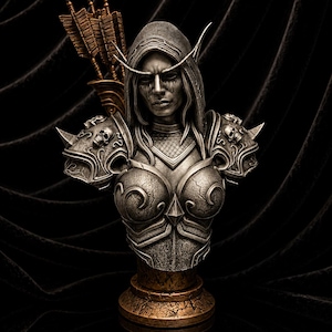 Pode incluir: Um busto prateado de uma figura arqueira com capuz, vestindo uma armadura ornamentada com motivos de caveiras nas ombreiras. A figura tem orelhas longas e pontiagudas, uma aljava com flechas nas costas e repousa sobre um pedestal de bronze.