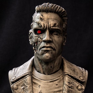 Pode incluir: Busto detalhado de um ciborgue com aparência metálica, com um olho vermelho brilhante e componentes mecânicos expostos em um lado do rosto. O busto está usando uma jaqueta de couro e uma camiseta de gola redonda, montado em uma base escura.
