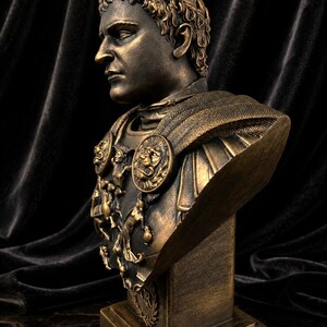 Pode incluir: Busto de cor bronze de um imperador romano, com tra&ccedil;os faciais detalhados e uma coroa de louros. O busto inclui uma armadura ornamentada com medalh&otilde;es de le&atilde;o e &eacute; montado sobre uma base retangular. Fundo escuro e texturizado.