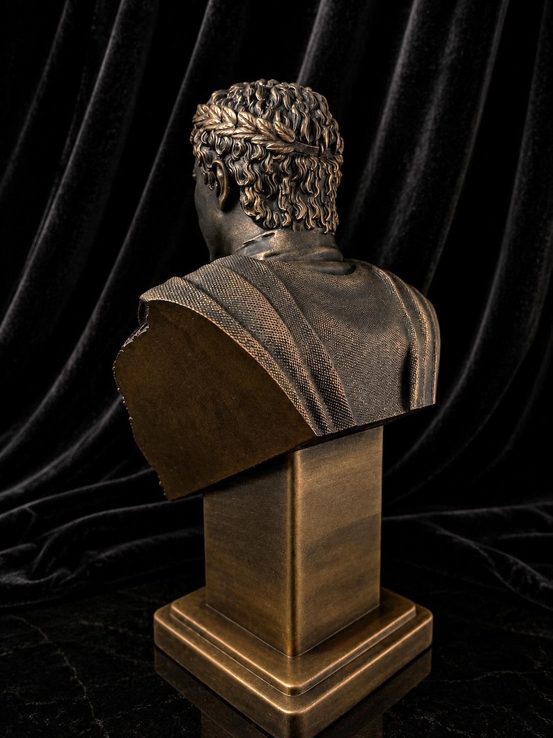 Pode incluir: Busto em bronze de um imperador romano, visto por tr&aacute;s. A escultura apresenta uma coroa de louros e texturas detalhadas no cabelo e nas roupas. O busto &eacute; montado em um pedestal quadrado.