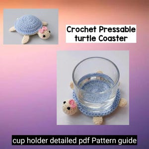 Pode incluir: Um porta-copos de tartaruga de crochê azul claro com um laço rosa claro e detalhes creme. O porta-copos está segurando um copo de água. O texto na imagem diz "Crochet Pressable turtle Coaster" e "cup holder detailed pdf Pattern guide".