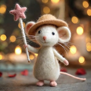 May include: A whimsical felt mouse figurine wearing a tan hat and holding a pink star wand. The mouse has a long pink tail and pink feet. The background features soft, blurred golden lights, creating a magical atmosphere.