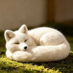 May include: A handcrafted white fox figurine curled up in a sleeping position. The fox is made of soft, textured material, with closed eyes and a black nose. It rests on a bed of green moss, creating a serene and natural scene.