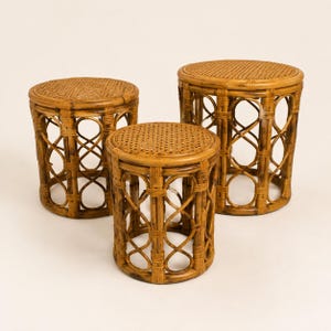 May include: A set of three round stools constructed from natural brown rattan. Each stool features a flat, woven circular top surface supported by a cylindrical base with an open, interlocking looped design and vertical structural supports.