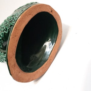 Puede incluir: La parte inferior de una maceta de cer&aacute;mica verde con un borde marr&oacute;n. La maceta tiene un acabado liso y brillante.