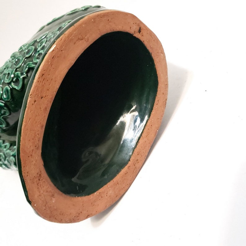 Puede incluir: La parte inferior de una maceta de cer&aacute;mica verde con un borde marr&oacute;n. La maceta tiene un acabado liso y brillante.