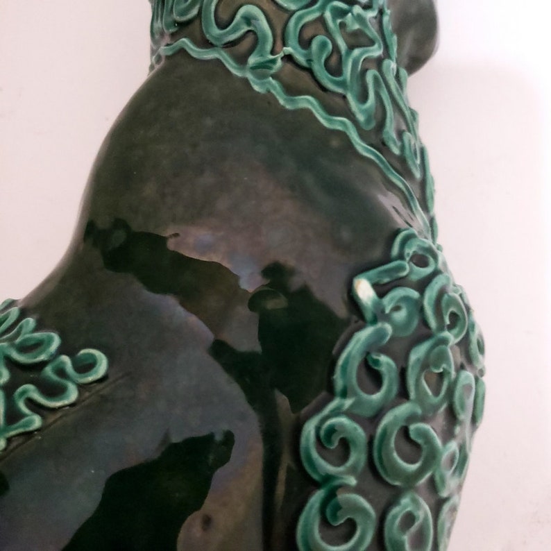 Puede incluir: Una escultura de cer&aacute;mica verde de un gallo con detalles intrincados. El gallo est&aacute; esmaltado en un color verde oscuro con un acabado brillante. La escultura tiene un dise&ntilde;o detallado de remolinos y l&iacute;neas verdes.