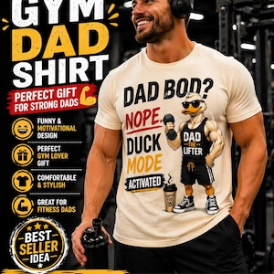 Puede incluir: Una camiseta beige con el texto "GYM DAD SHIRT" y un pato de dibujos animados levantando pesas. La camiseta también presenta las frases "DAD BOD? NOPE DUCK MODE ACTIVATED" y "COFFEE FUEL DAD".