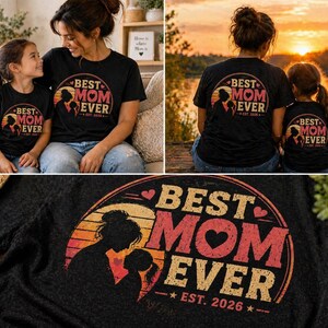 K&ouml;nnte beinhalten: Schwarze T-Shirts mit dem Aufdruck "BEST MOM EVER" in Orange und Rot, mit einer Silhouette von Mutter und Kind. Der Text "EST. 2026" ist ebenfalls enthalten. Die Shirts werden von einer Mutter und ihrer Tochter getragen. Das Design ist kreisf&ouml;rmig.