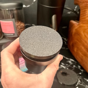 May include: A black grinder with a gray rubber base. The grinder is being held in a hand.