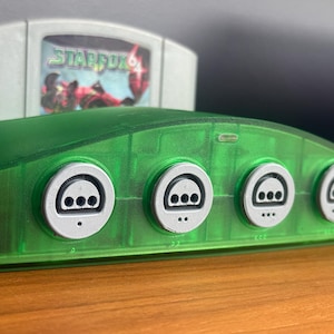 May include: A transparent green Nintendo 64 console with four controller ports and a Star Fox game cartridge. The console has a curved design with white controller port covers. The Star Fox cartridge is light gray with colorful graphics.