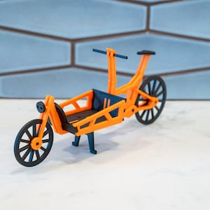 May include: A 3D printed model of an orange cargo bike with black wheels and handlebars. The bike has a cargo box in the back and a stand.