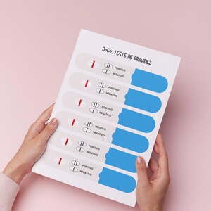 以下が含まれることがあります： 「Jogo: Teste de Gravidez」の文字と妊娠検査薬のイラストが描かれた白い紙。各検査薬は赤い線を示し、陽性結果を示しています。ピンク色の背景に紙が保持されています。