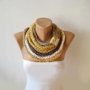 May include: A multi-coloured crocheted infinity scarf in shades of white, grey, and yellow. The scarf is worn around a mannequin's neck.