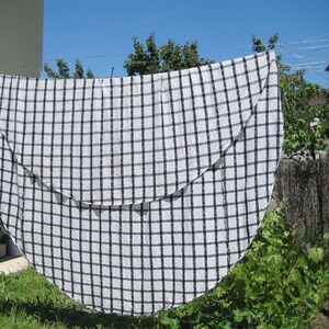 May include: A white tablecloth with a black checkered pattern is hanging on a washing line. The tablecloth is folded in half, creating a semi-circular shape.