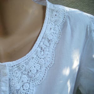 May include: White blouse with a detailed, openwork lace collar. The collar is a prominent feature, with intricate floral and geometric patterns. The blouse has a button-down front and a simple, classic design, suitable for various occasions.