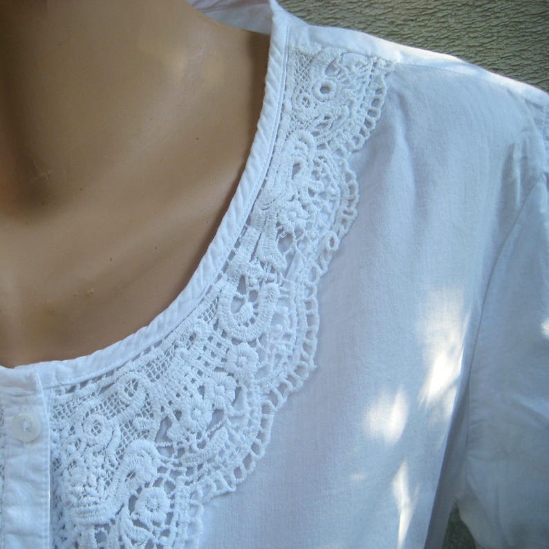May include: White blouse with a detailed, openwork lace collar. The collar is a prominent feature, with intricate floral and geometric patterns. The blouse has a button-down front and a simple, classic design, suitable for various occasions.