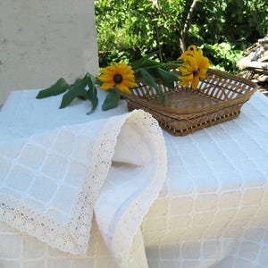 Pu&ograve; includere: Tovaglia di lino bianco con un bordo di pizzo e un cesto intrecciato con fiori gialli in cima.