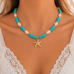 Può includere: Una collana con un ciondolo a forma di stella marina color oro sospeso a una fila di perline alternate color turchese e perline bianche testurizzate simili a conchiglie, arricchita da piccoli distanziatori sferici color oro.