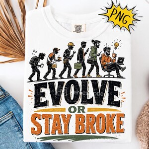 May include: A white t-shirt featuring a graphic illustration of human evolution from a student to a professional working at a desk. Below the figures, the text reads EVOLVE OR STAY BROKE in large black and orange letters. The shirt has a crew neck.