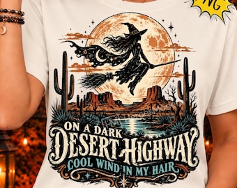 May include: A white t-shirt featuring a graphic of a witch flying on a broomstick in front of a large moon over a desert landscape with cacti and mesas. The text reads ON A DARK DESERT HIGHWAY COOL WIND IN MY HAIR in black and blue lettering.