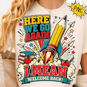 May include: A cream-colored t-shirt featuring a graphic print of a yellow pencil rocket ship launching amidst books, red apples, and paper airplanes. The text reads: HERE WE GO AGAIN I MEAN WELCOME BACK! The design includes colorful stars and clouds.