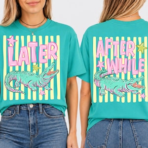 May include: Teal t-shirts with a playful design. The front of the shirt says "LATER" in pink letters, with a green alligator graphic and yellow and white stripes. The back says "AFTER WHILE" with the same alligator graphic.