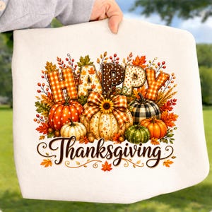 May include: A white fabric item featuring a colorful graphic of pumpkins, autumn leaves, and berries. The text HAPPY THANKSGIVING is printed in a decorative font. The pumpkins are decorated with plaid, polka dot, and solid patterns.